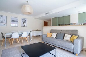 Una sala de estar moderna con un sofá gris, una mesa de centro negra y un comedor con mesa y sillas de vidrio.