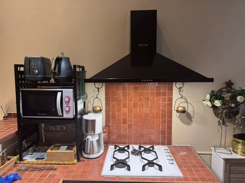 Een keuken met een gasfornuis, een magnetron, een koffiezetapparaat en een zwarte afzuigkap.