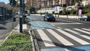 Un passage piéton avec une bande bleue peinte au sol, un feu de signalisation et un immeuble à plusieurs étages en arrière-plan.