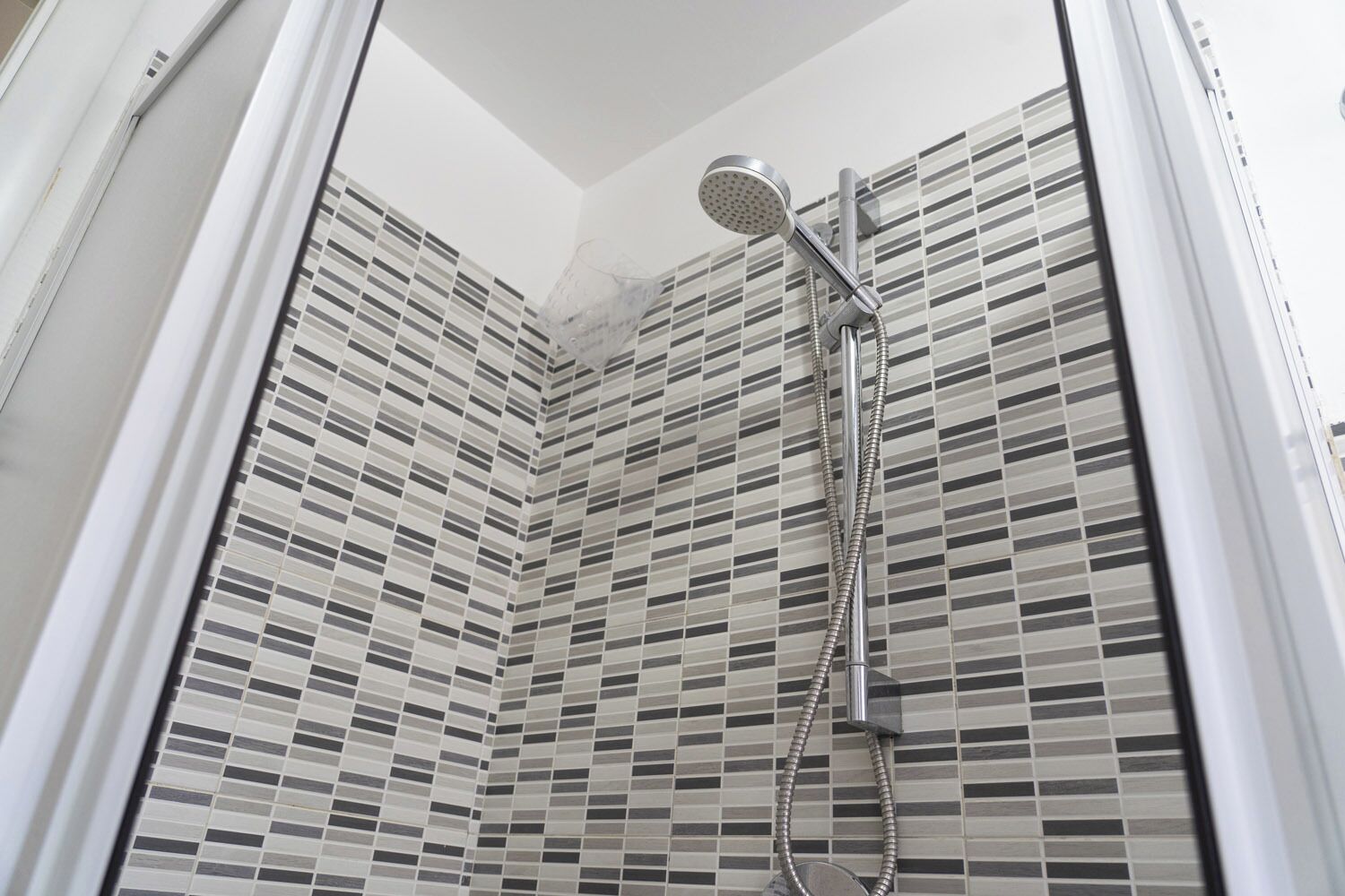 Une douche équipée d’un pommeau de douche à main et d’un flexible, installée devant un mur carrelé à motifs à carreaux.
