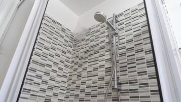 Une douche équipée d’un pommeau de douche à main et d’un flexible, installée devant un mur carrelé à motifs à carreaux.