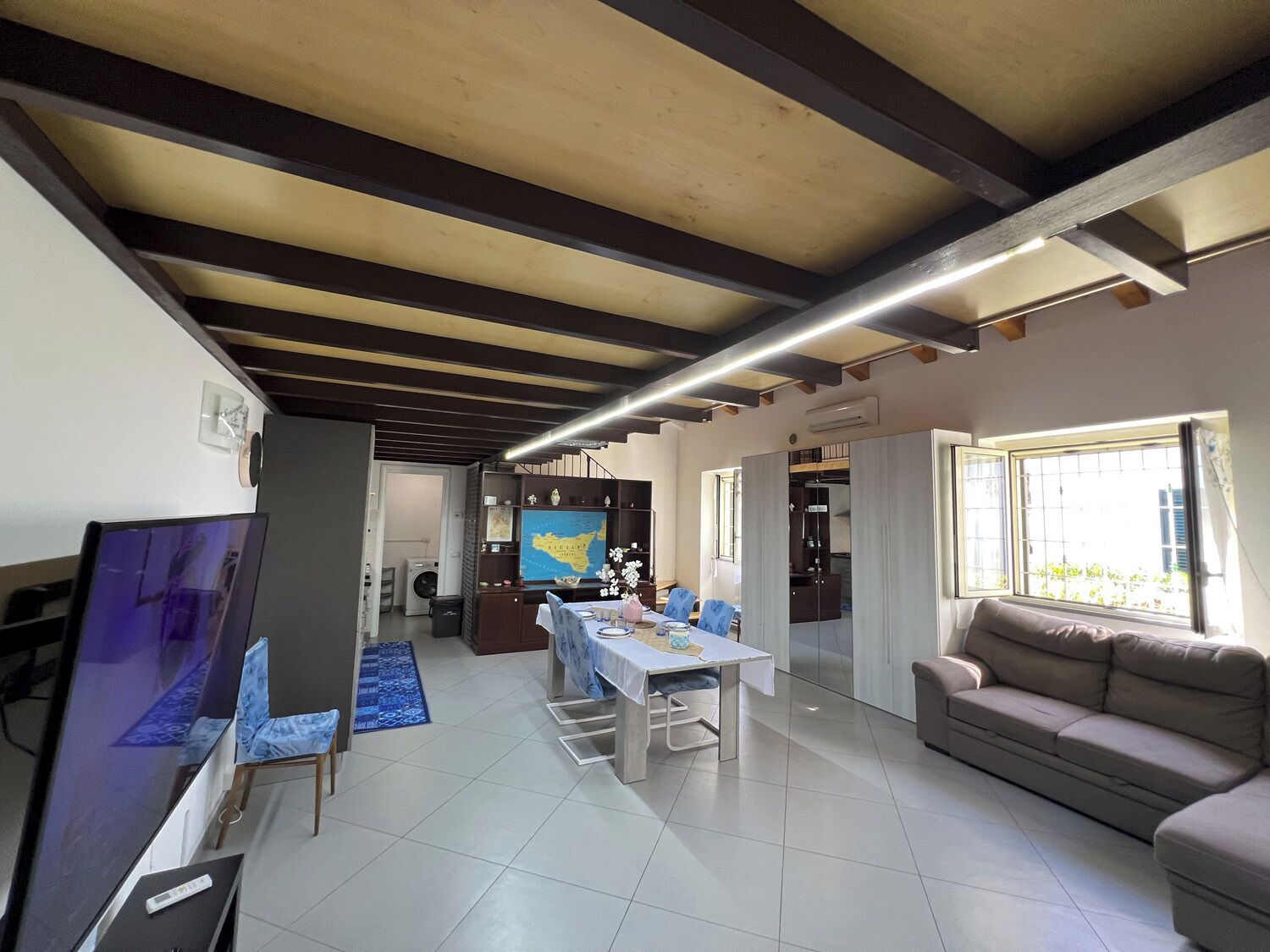A modern living room with a dining area, a sofa, a TV, and a map on the wall.