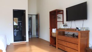 Quarto com uma secretária de madeira, televisão e guarda-roupa. Uma porta dá acesso a uma casa de banho.