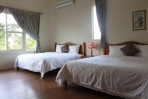 A hotel room with two beds, a wooden floor, and a window with curtains.