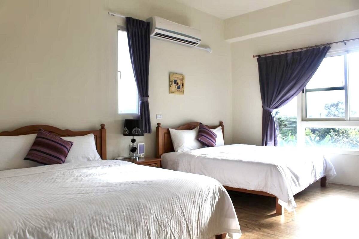 Habitación de hotel con dos camas, una mesita de noche, un equipo de aire acondicionado y una ventana con cortinas.