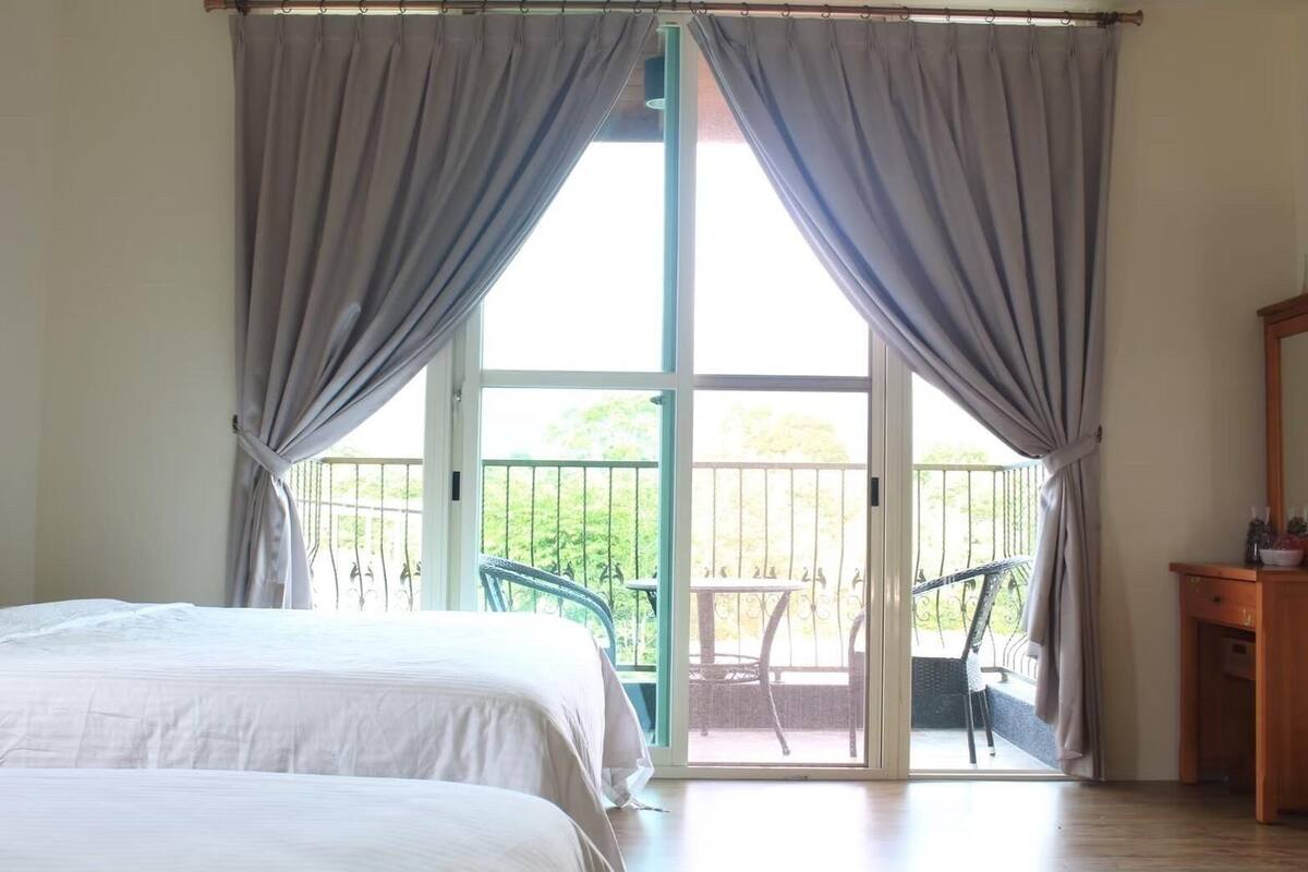 Un dormitorio con una cama grande, un balcón con sillas y un aparador de madera.