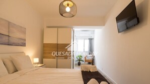 A modern hotel room with a large bed, a flat-screen TV mounted on the wall, and a view of the outside through a sliding door.