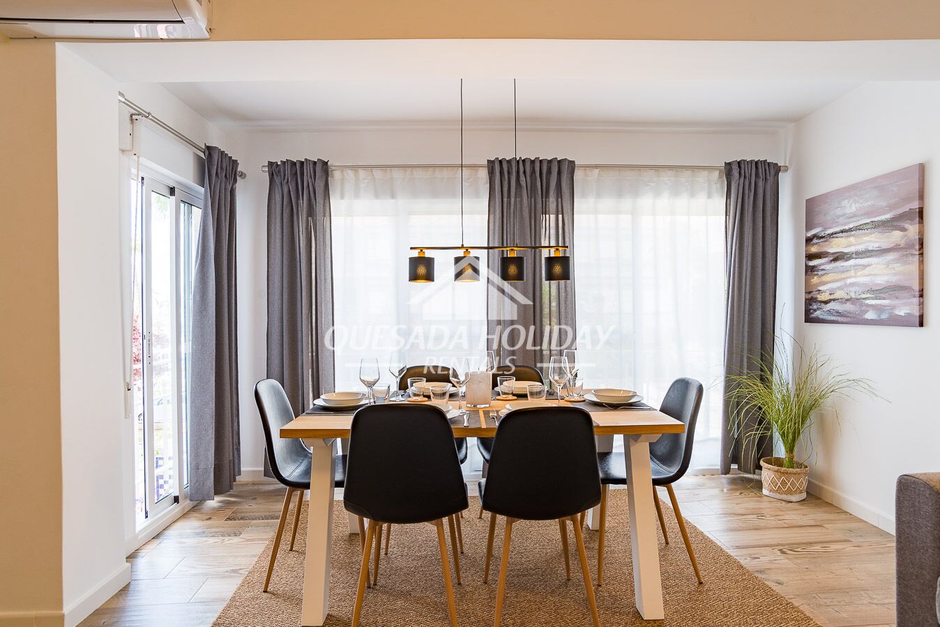 Un comedor con mesa de madera, sillas negras y una lámpara colgante.
