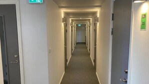 Pasillo de hotel con varias puertas, señales de salida de emergencia y suelo alfombrado.