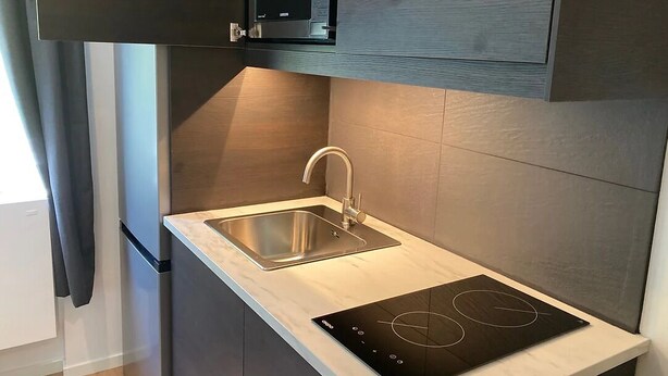 Una cocina moderna con microondas integrado, pileta de acero inoxidable y cocina por inducción.