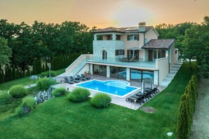 Une maison moderne à deux étages, dotée d’une piscine, d’un patio couvert et d’un jardin bien entretenu.