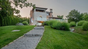 Une maison moderne avec une façade en pierre, un chemin pavé menant à l’entrée et une pelouse bien entretenue.