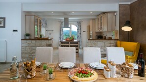 Un coin repas avec une table en bois dressée pour le repas, des chaises et, au fond, une vue sur la cuisine.