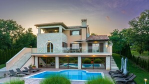 Une maison moderne à deux étages, dotée d’une piscine, d’un espace salon extérieur et d’un jardin bien entretenu.