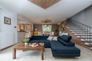 Una sala de estar moderna con un sofá seccional, una mesa de centro de madera y una escalera con barandal negro.