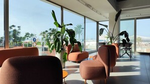 A modern lounge area with large windows, comfortable seating, and potted plants. - Hotel Sporting (Riccione)