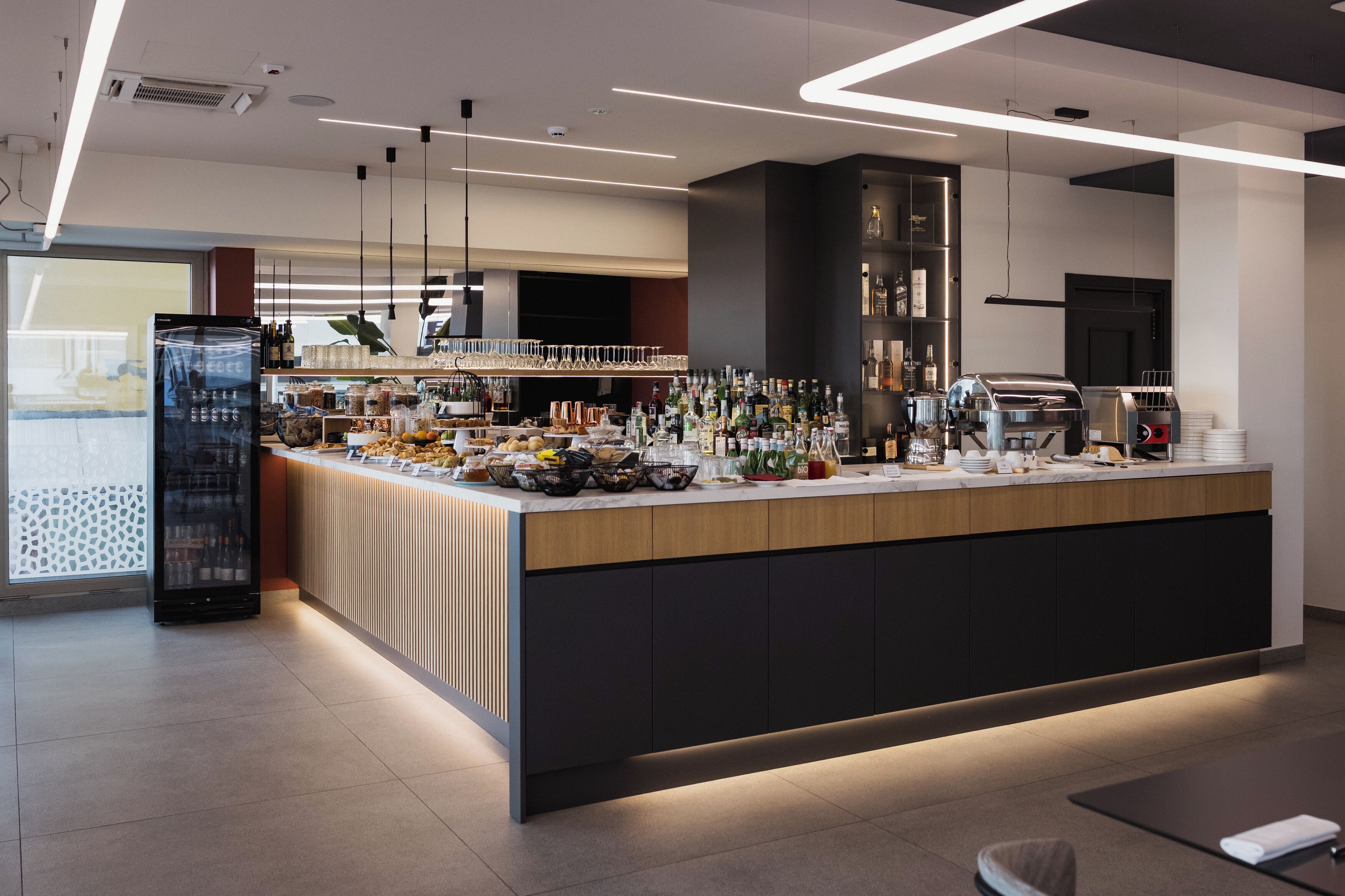 Een moderne bar met een gebogen toonbank, verschillende flessen, glazen en een koffiemachine.