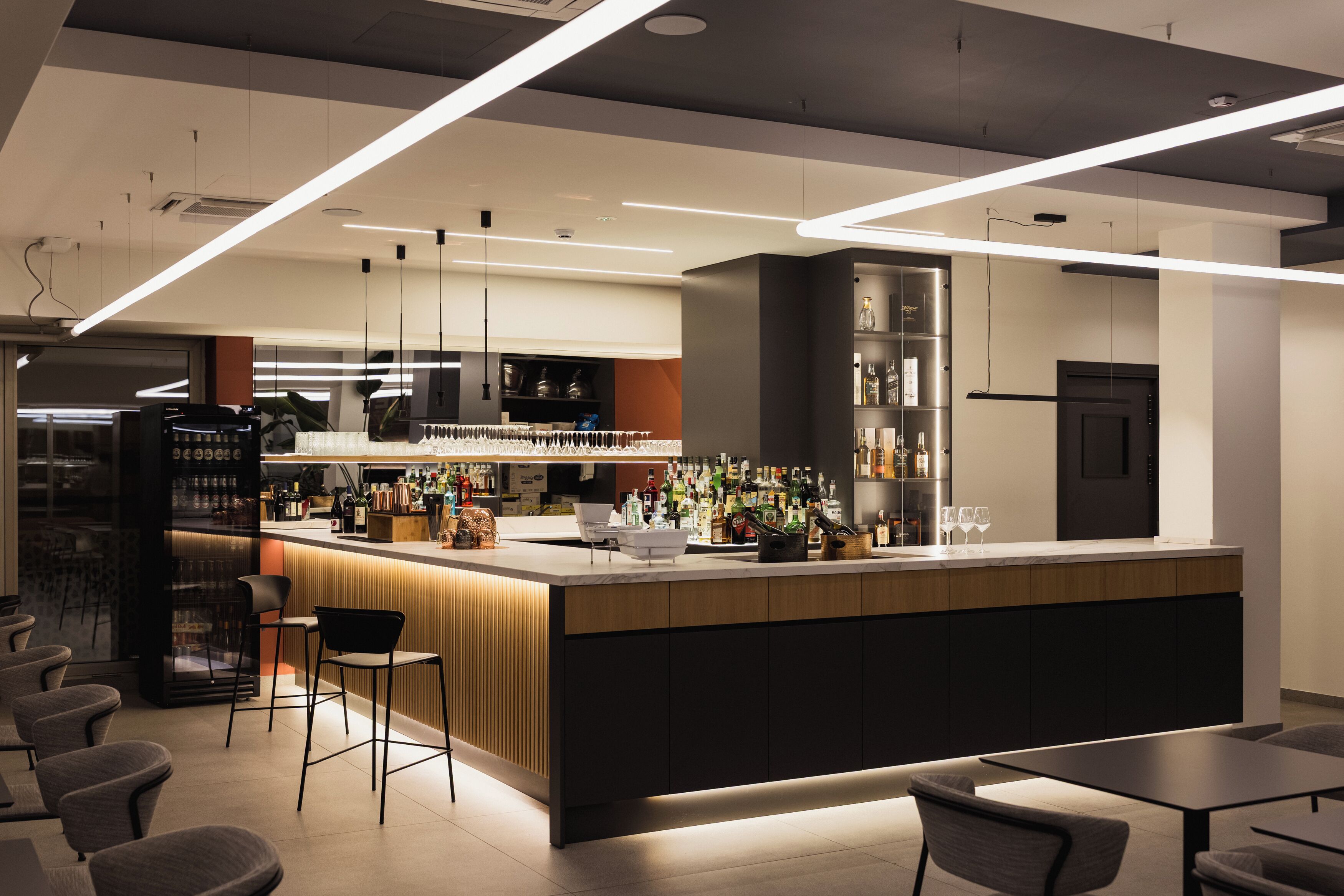 A modern bar area with a counter, stools, and a variety of bottles.