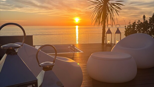 A wooden deck with white cushioned seating and lanterns, overlooking a sunset over the sea. - Hotel Sporting (Riccione)