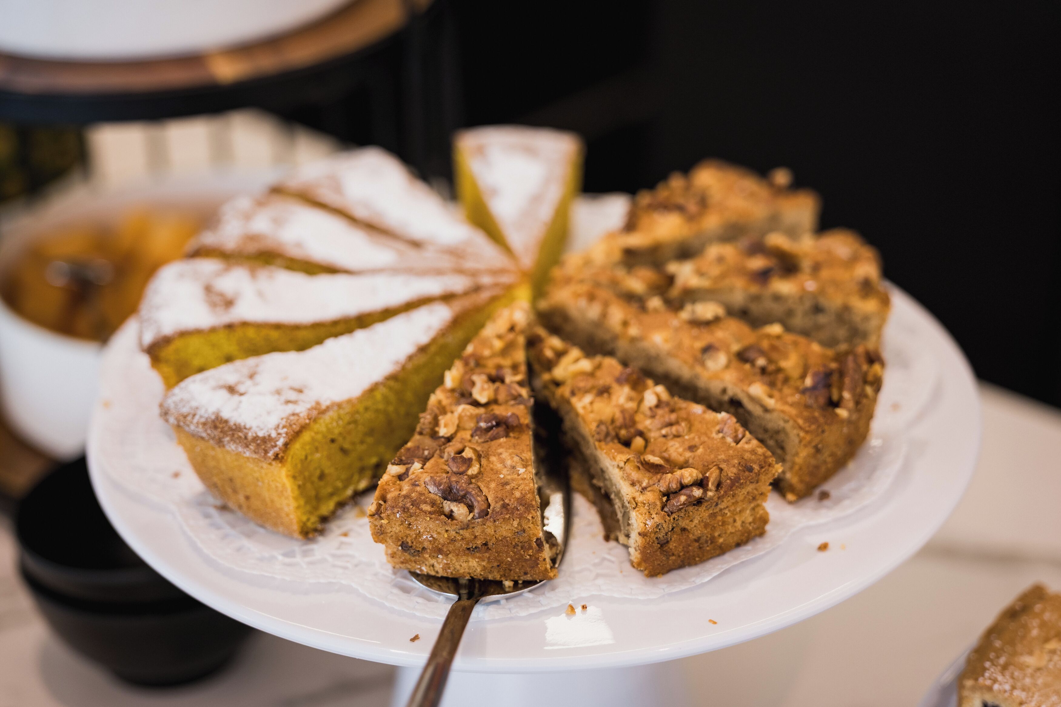 Una porción de pastel con un poco de azúcar glas y nueces picadas sobre un plato blanco.