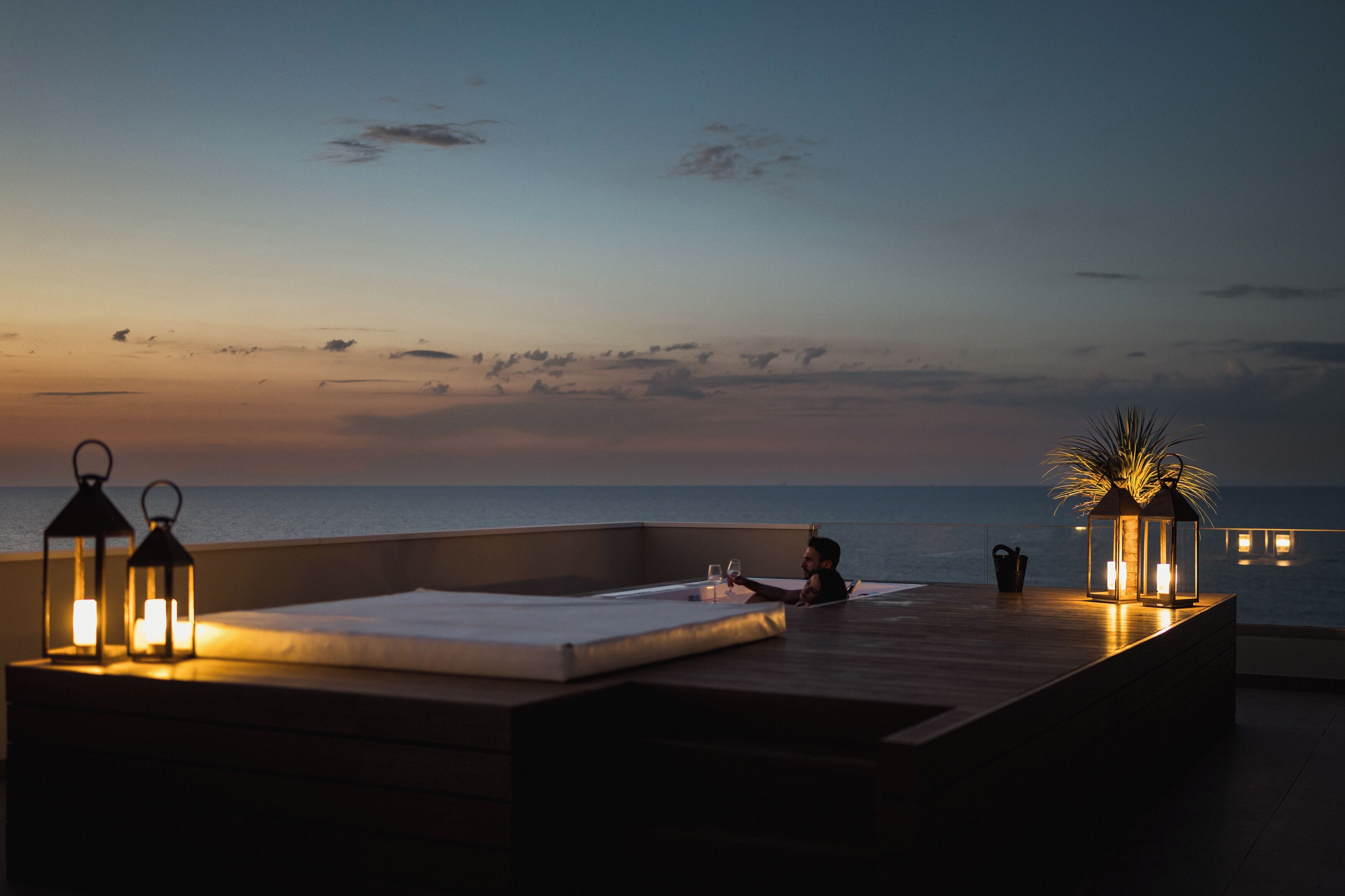 A rooftop terrace with a view of the sea, equipped with seating and lanterns.