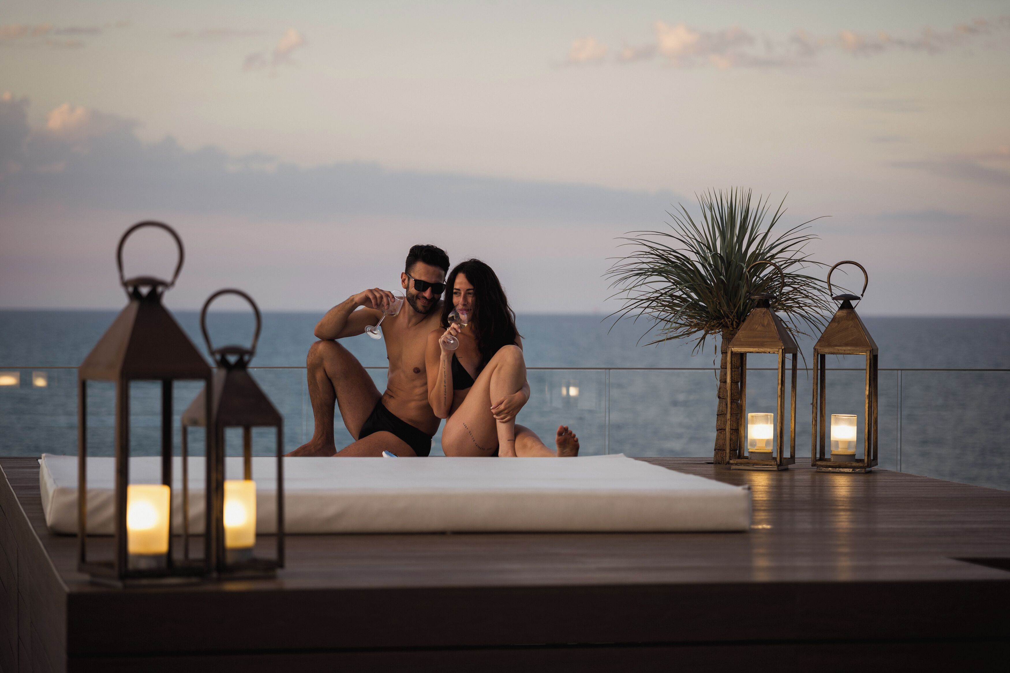 A couple sitting on a deck with a view of the sea, surrounded by lanterns and candles.