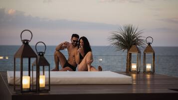 A couple sitting on a deck with a view of the sea, surrounded by lanterns and candles.