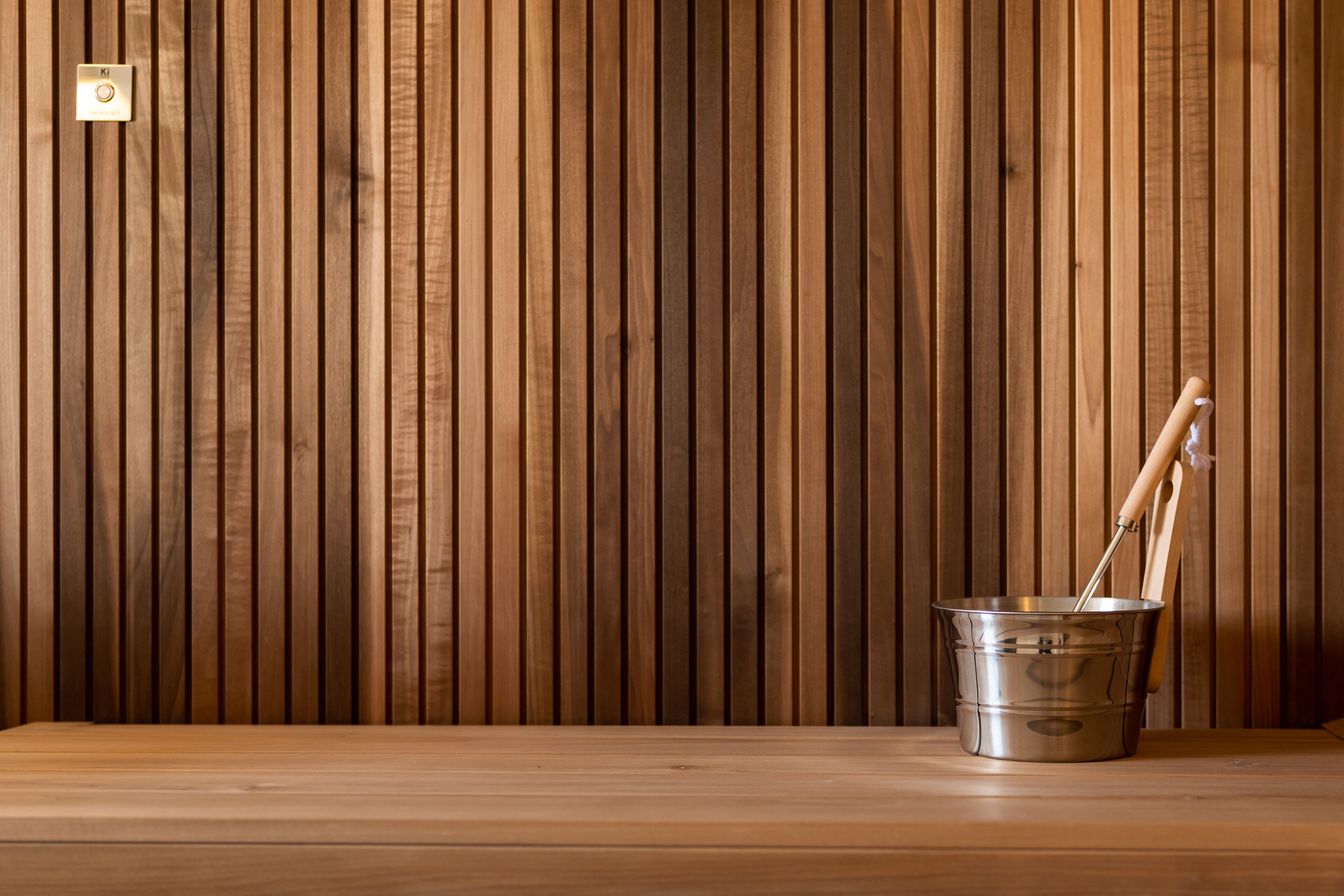 Pared de paneles de madera con un balde de metal y herramientas de mango de madera sobre un suelo de madera.