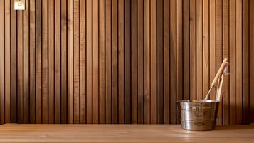 Pared de paneles de madera con un balde de metal y herramientas de mango de madera sobre un suelo de madera.
