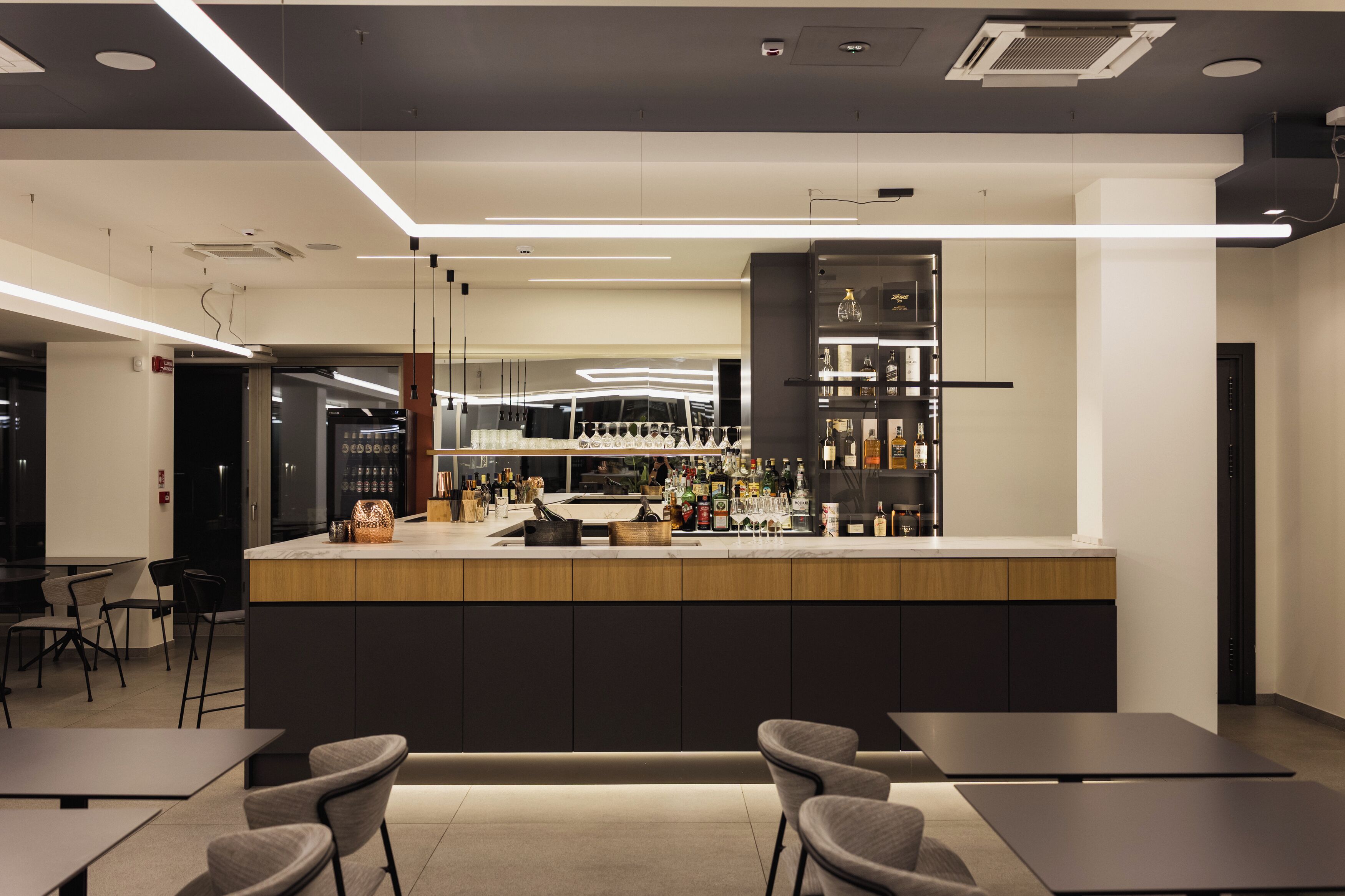 A modern bar area with a counter, seating, and a variety of bottles and glasses.