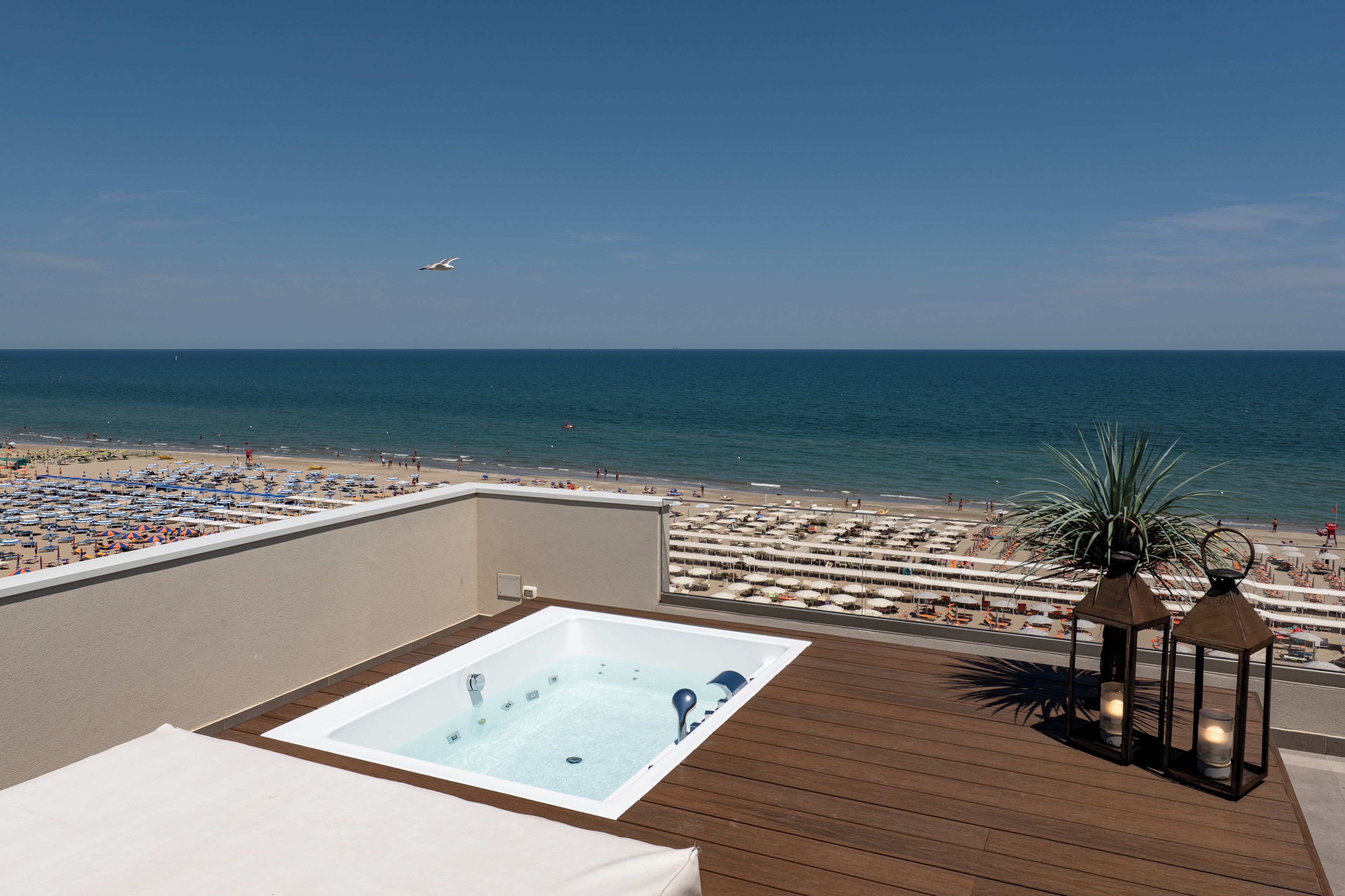 Terraza en la azotea con jacuzzi, con vistas a una playa que tiene sombrillas y tumbonas.