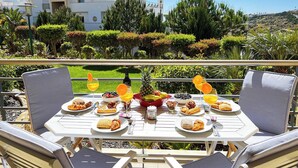 Ein Essbereich im Freien mit einem für das Frühstück gedeckten Tisch, umgeben von Stühlen und mit Blick auf einen angelegten Garten sowie ein modernes Gebäude.