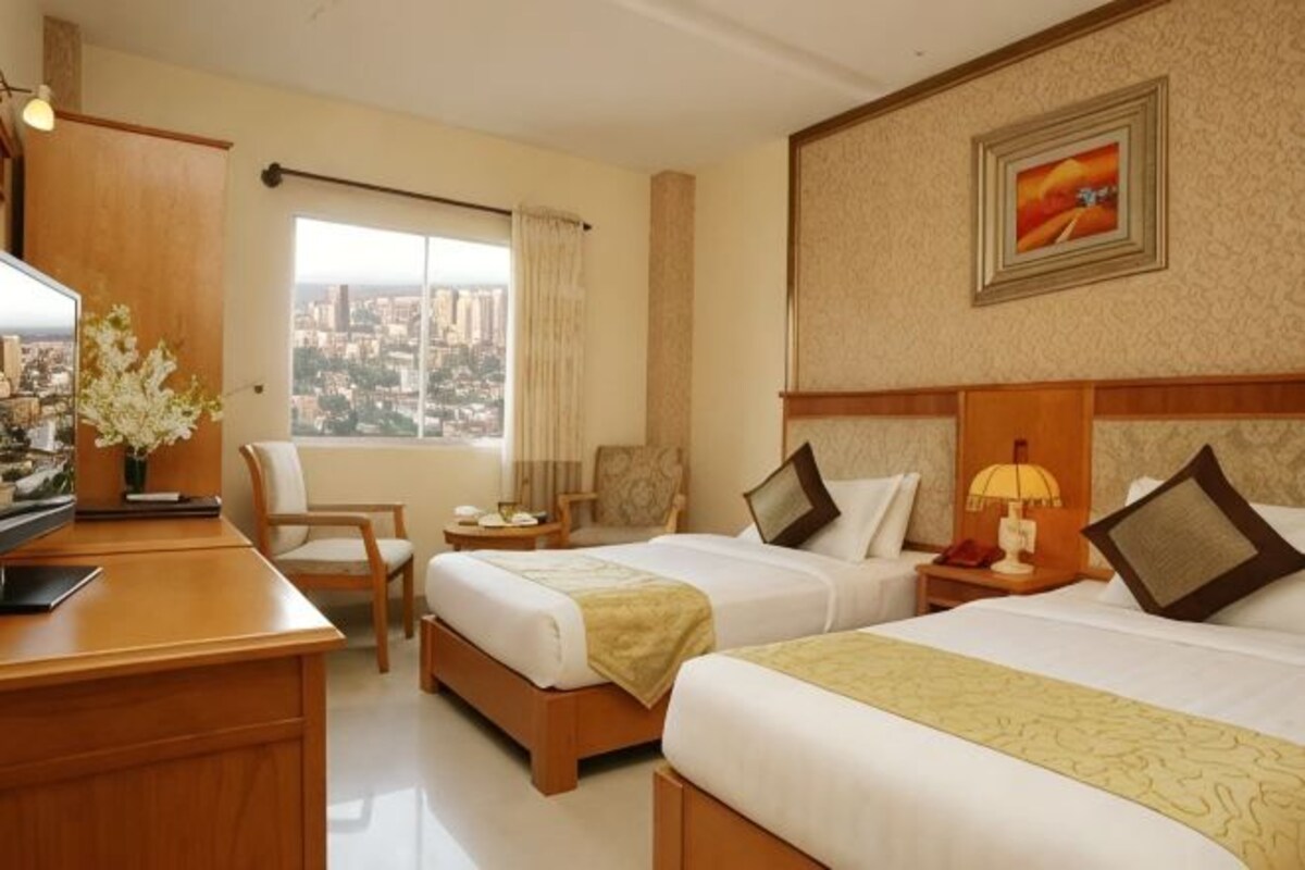 A hotel room with two beds, a desk, a chair, a television, and a window with a city view.