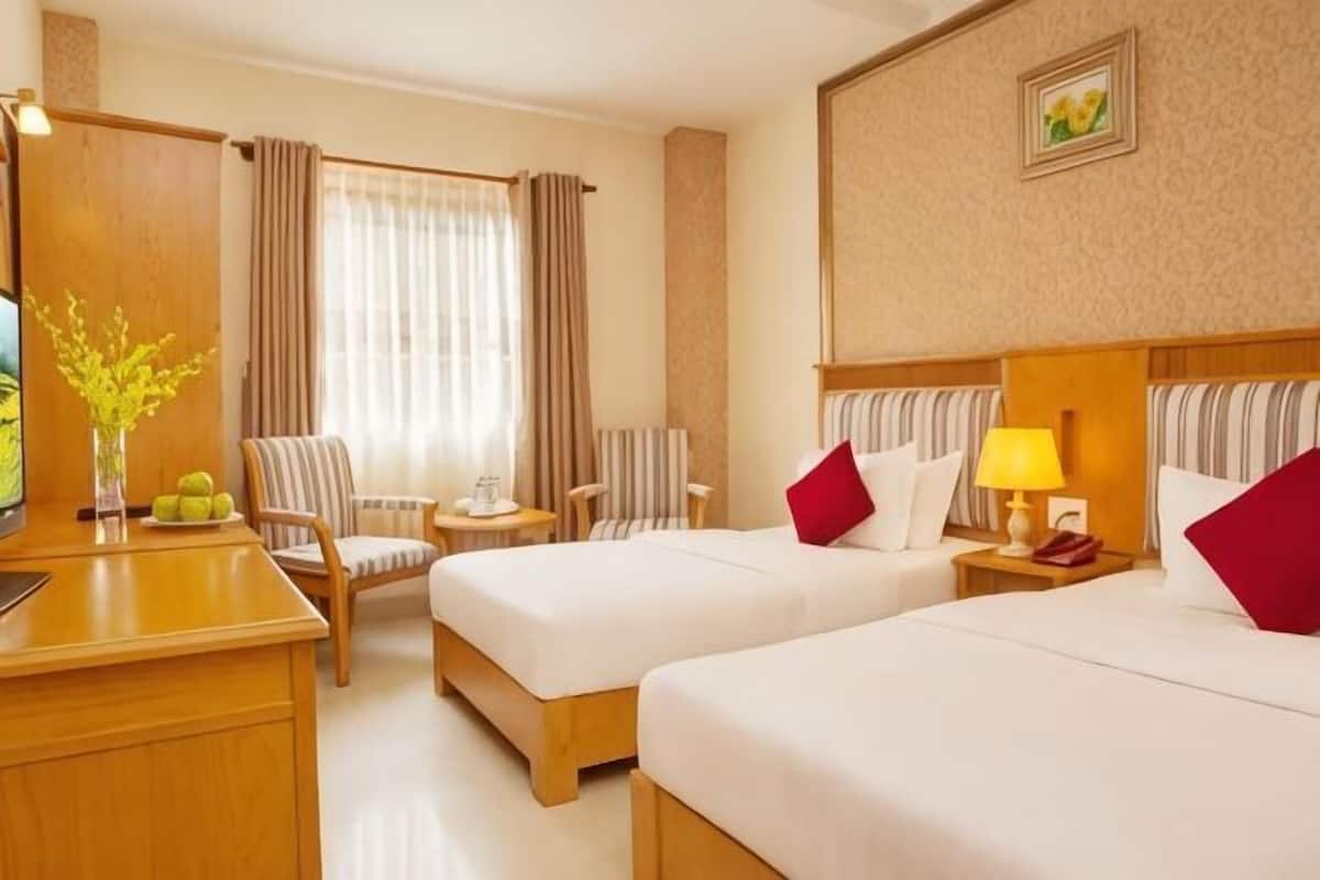 A hotel room with two beds, a desk, a chair, a small table, and a window with curtains.