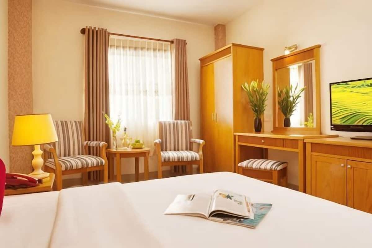 A hotel room with a bed, a TV, a desk with a chair, a small table with a lamp, and two chairs.