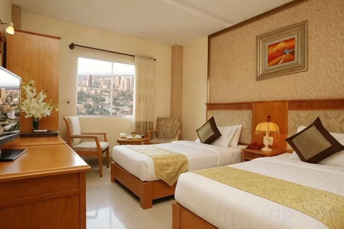 Habitación de hotel con dos camas, un escritorio, una silla, un televisor y vistas a la ciudad.