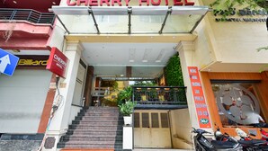 L’entrée de l’hôtel Cherry, avec un escalier menant à l’entrée, une enseigne indiquant la présence d’une salle de billard, et une moto garée à l’extérieur.