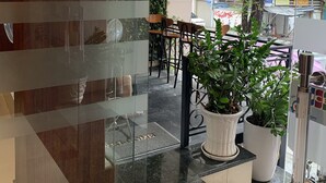 Un espace intérieur moderne, doté d’une cloison en verre, d’un comptoir d’accueil et d’un coin salon avec des chaises et une table. Des plantes en pot sont disposées dans l’espace, et la vue sur l’extérieur est bien visible à travers le verre.