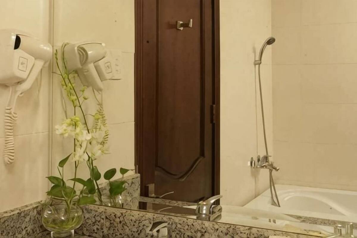 A bathroom with a hairdryer, a door, a shower, and a sink with a mirror.