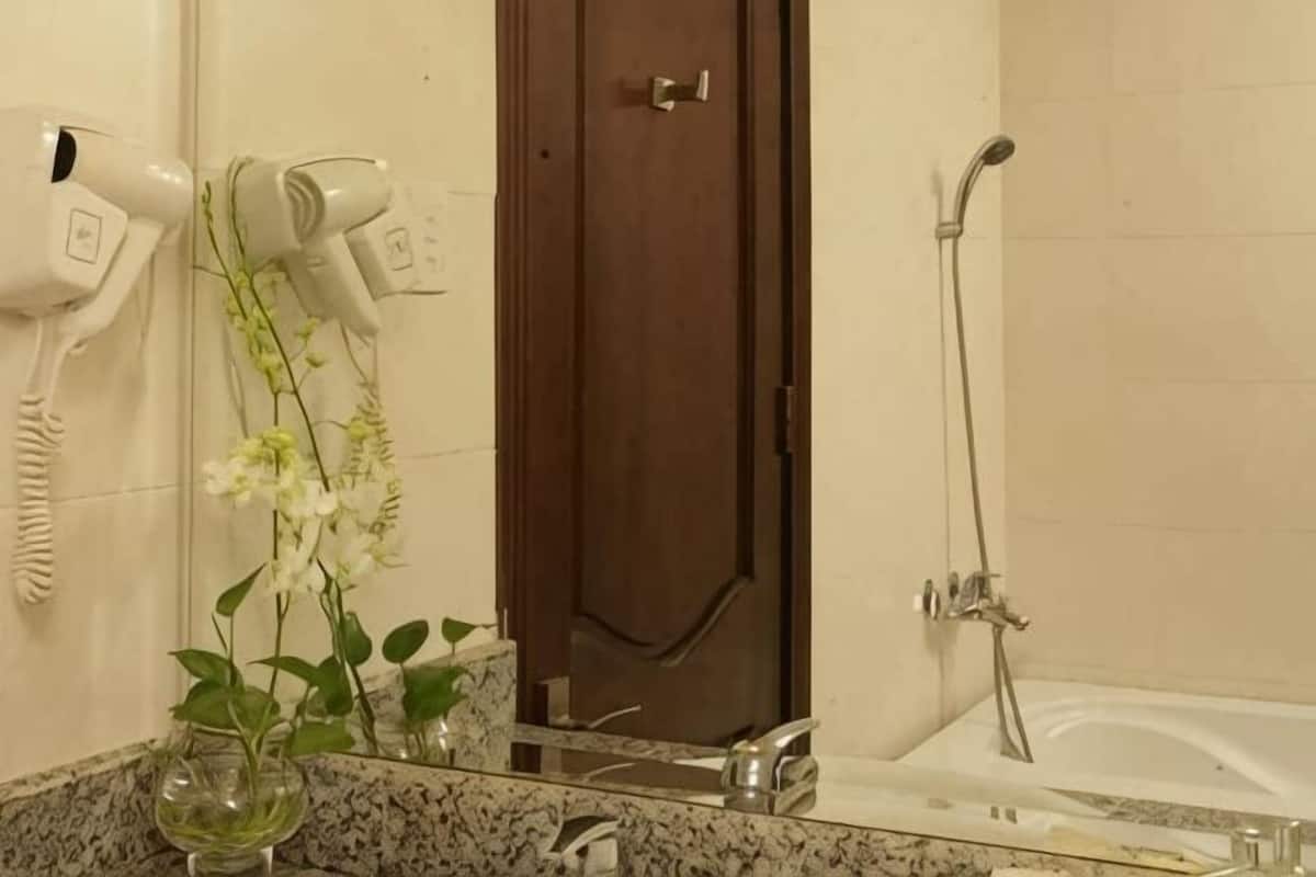 Un baño con secador de pelo, puerta, ducha y lavabo con espejo.