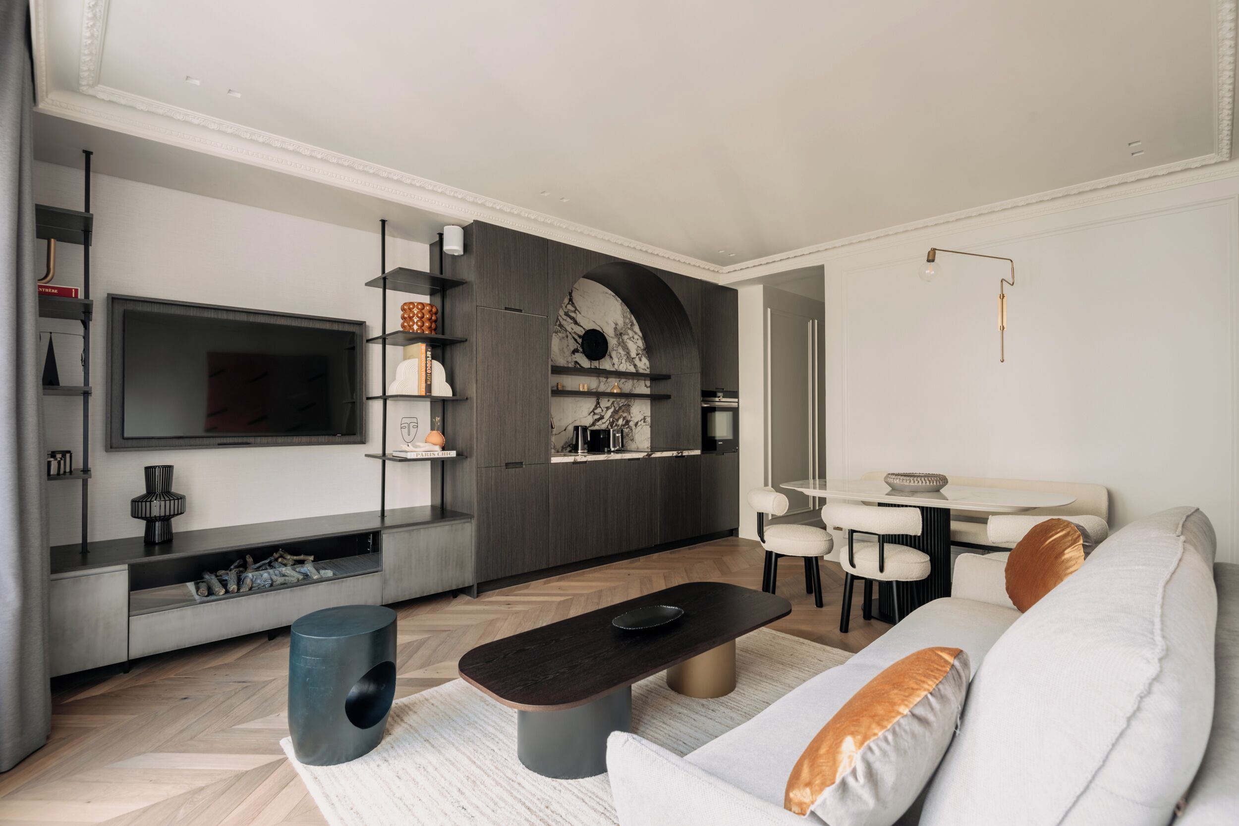 Una sala de estar moderna con un televisor de pantalla plana, una mesa de centro oscura, un sofá con cojines, un comedor con mesa y sillas, y una cocina con salpicadero de mármol.