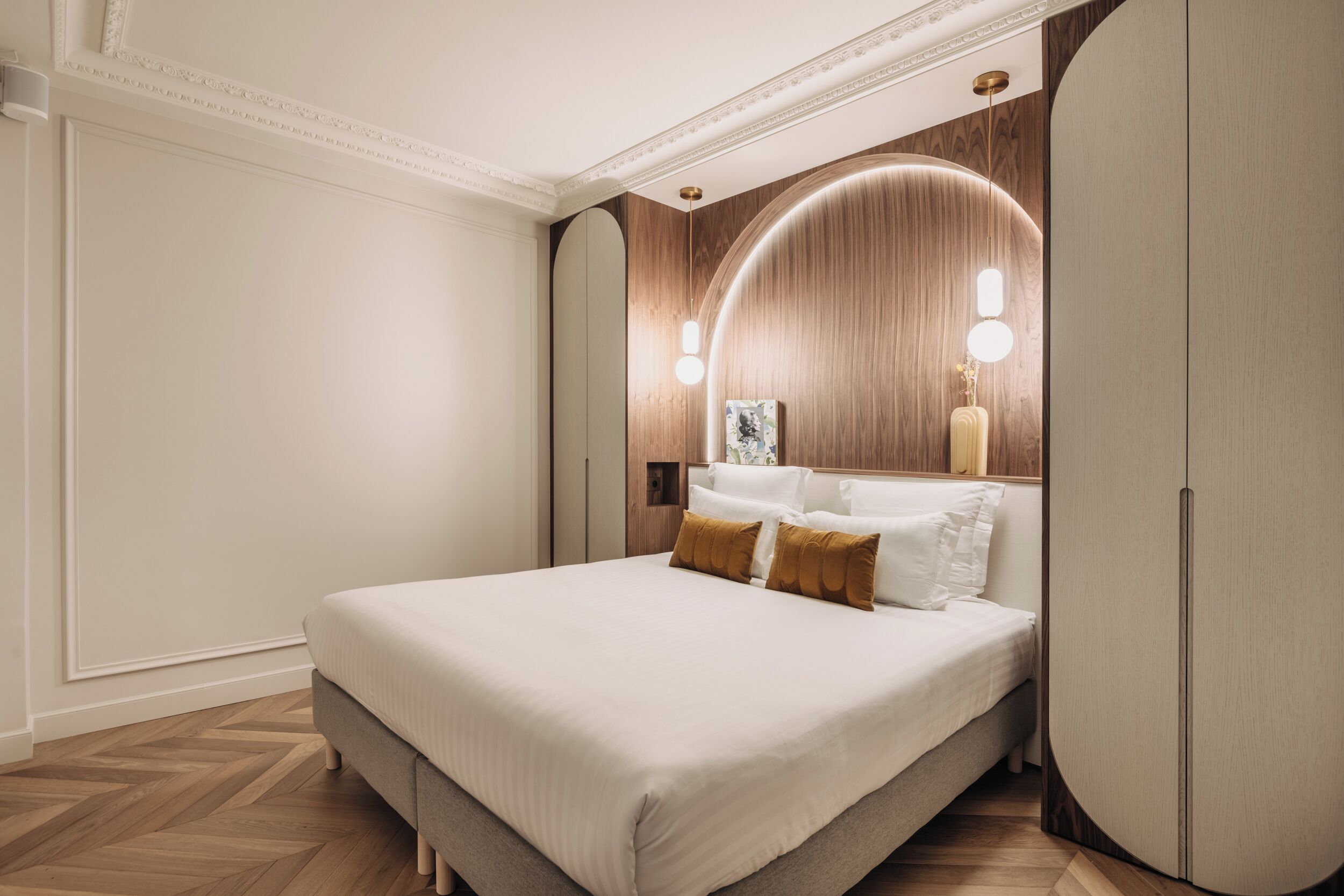 Ein modernes Schlafzimmer mit einem großen Bett, Holzvertäfelung an den Wänden und einer gebogenen Deckenleuchte.