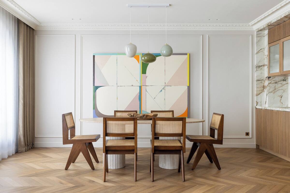 A dining area with a wooden herringbone floor, a central table with four chairs, and a large abstract painting on the wall.
