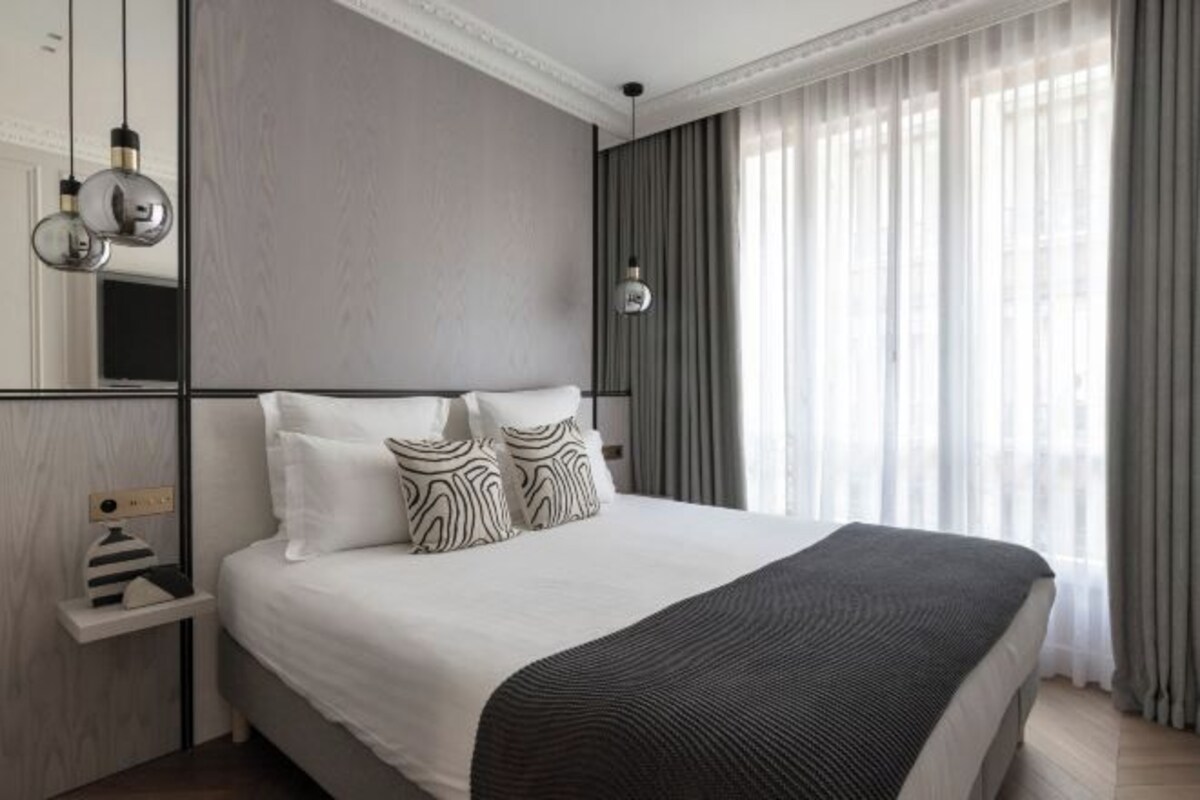 Quarto de hotel moderno com uma cama grande, mesa de cabeceira e espelho.