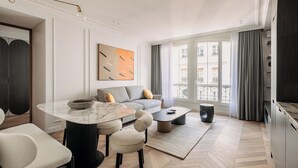 A modern living room with a marble coffee table, grey sofa, and a large window with curtains. - HIGHSTAY - Luxury Serviced Apartments - Centre Pompidou Museum (Paris)