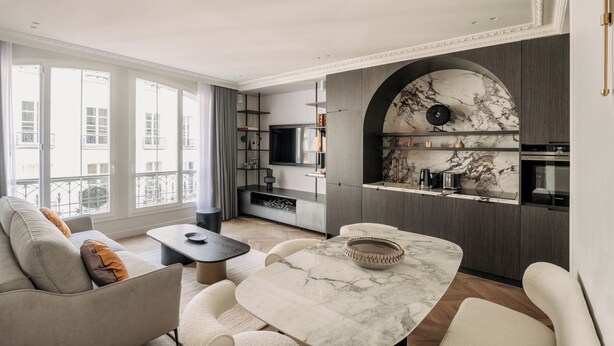 A modern living room with a marble table, sofa, and a kitchen area with a built-in oven and TV. - HIGHSTAY - Luxury Serviced Apartments - Centre Pompidou Museum (Paris)