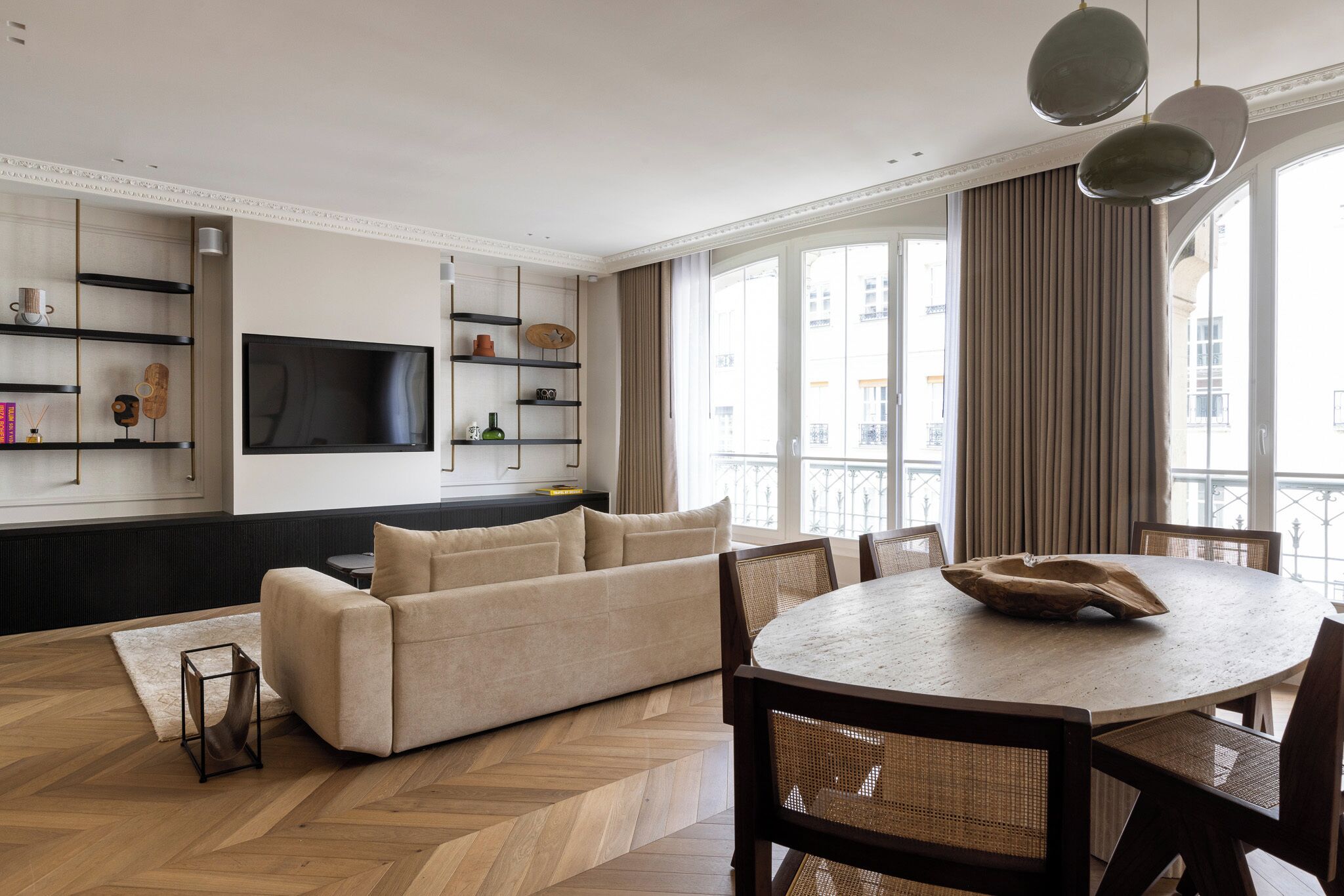 Una sala moderna con sofá, mesa de comedor y sillas. Hay un televisor de pantalla plana montado en la pared y una ventana con cortinas.