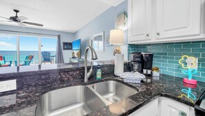 Una cucina moderna con un lavello doppio, una ventola a soffitto e vista sull'oceano attraverso ampie finestre.