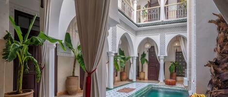 An indoor courtyard with a pool, potted plants, and a traditional Moroccan architectural style.