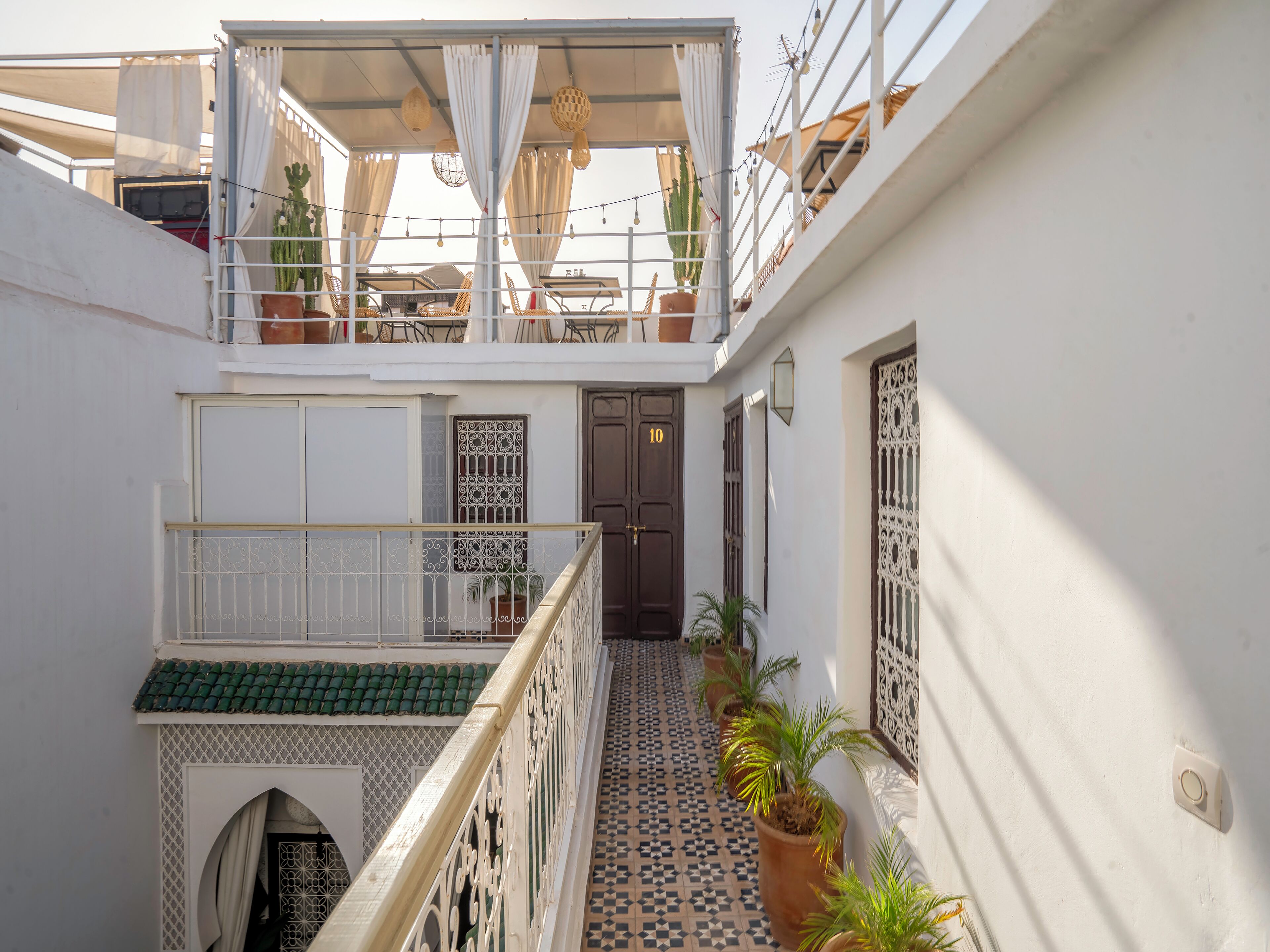 A courtyard with a tiled floor, a balcony with a railing, and potted plants.